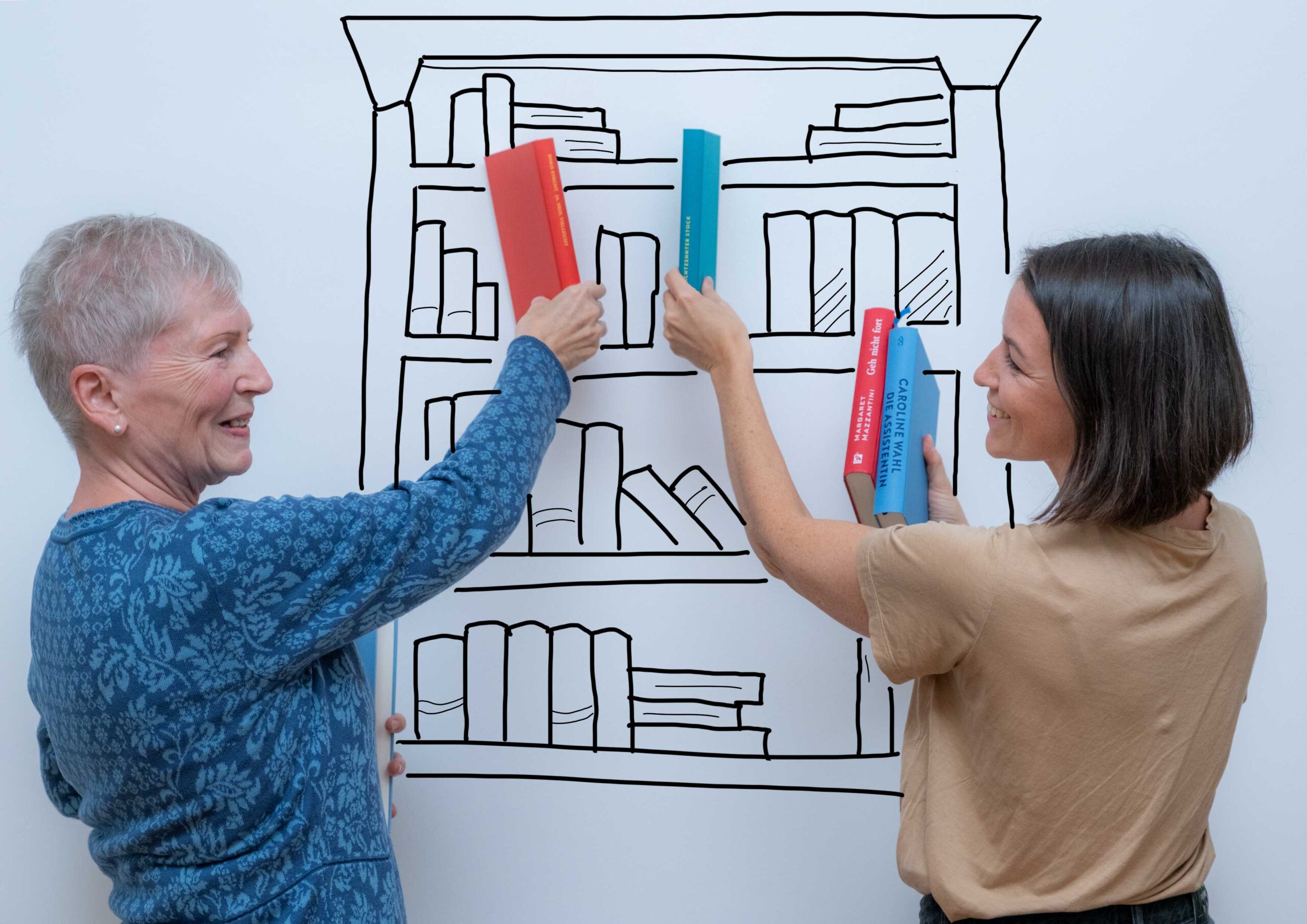 Zwei Personen stellen Bücher in ein aufgemaltes Bücherregal