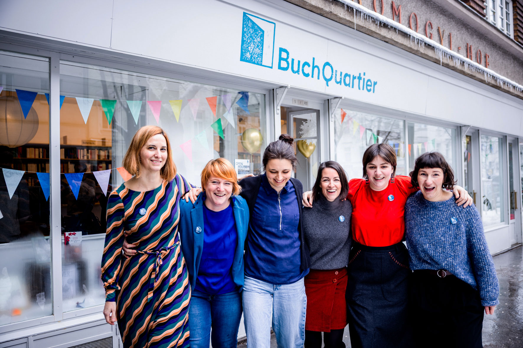 BuchQuartier Team beim gemeinsamen Austausch vor der Buchhandlung, hinter ihnen sind das Schaufenster und Bücherregale zu sehen.