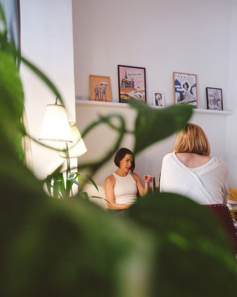 Zwei Frauen unterhalten sich an einem Tisch im BuchQuartier-Café, im Vordergrund sind grüne Pflanzen zu sehen