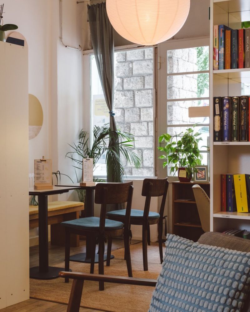 Gemütlicher Sitzbereich mit Holztischen, Stühlen, Büchern und Pflanzen im Café des BuchQuartiers
