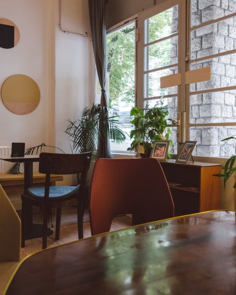 Heller Sitzplatz mit Holztisch, Stühlen und Pflanzen am Fenster des BuchQuartier-Cafés