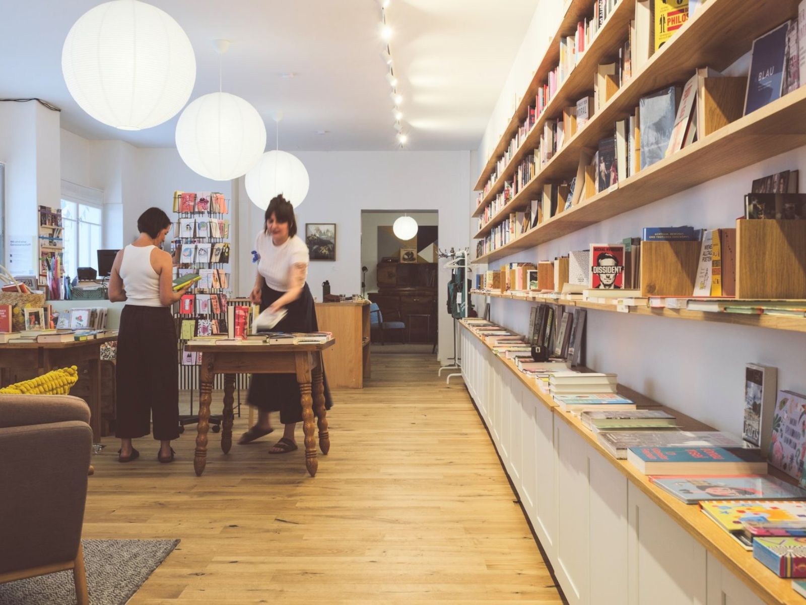 Heller Veranstaltungsraum des BuchQuartiers mit Bücherregalen, Holztischen und zwei Personen beim Vorbereiten des Raums