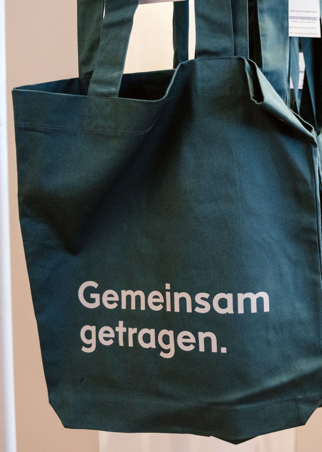 Blaue BuchQuartier-Stofftasche mit der weißen Aufschrift „Gemeinsam getragen“ vor einem Fenster